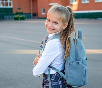 girl in a uniform and blue backpack smiling