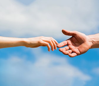 two hand reaching for one another with sky background