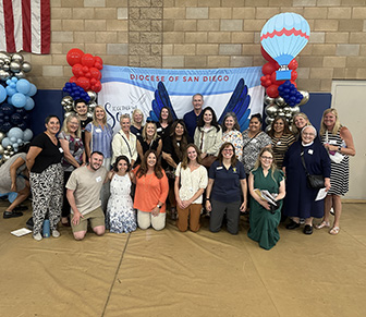 staff standing and kneeling in front of balloons and a sign that reads welcome back