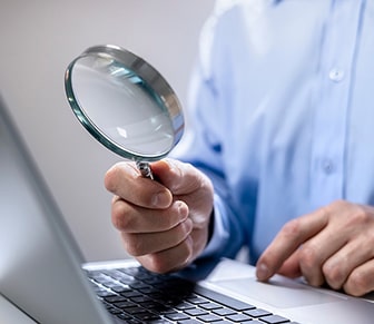 person holding a magnify glass by a laptop