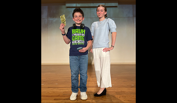 Two student actors on stage with one holding up golden ticket