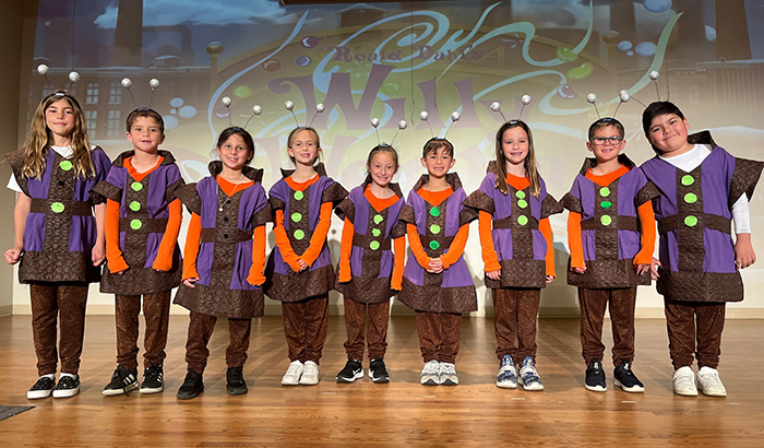 Group of student actors on stage in purple and brown costumes