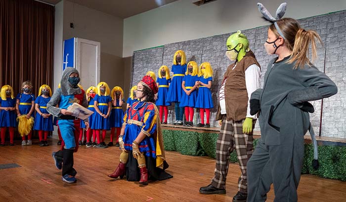 Lord Farquaad and Knight talking with Shrek and Donkey surrounded by dancers in blue dresses and yellow wigs